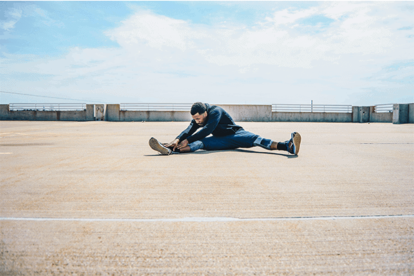 man wearing blue sweater and gray pants sitting and stretching legs