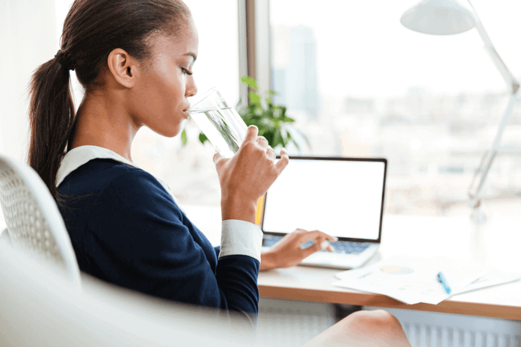woman sitting in a chair at her desk, drinking a glass of water