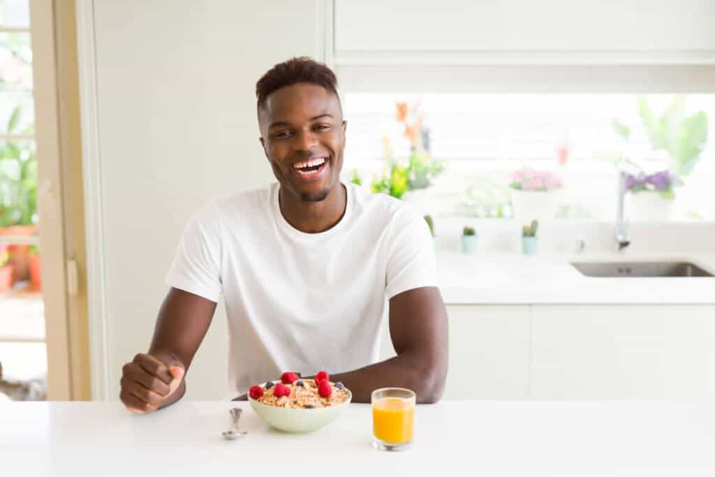 man sitting at kitchen table eating fruit and drinking orange juice