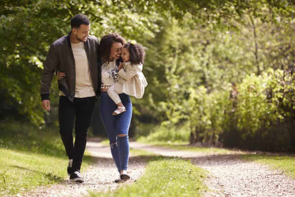Family of three walking in a park with mother holding child.