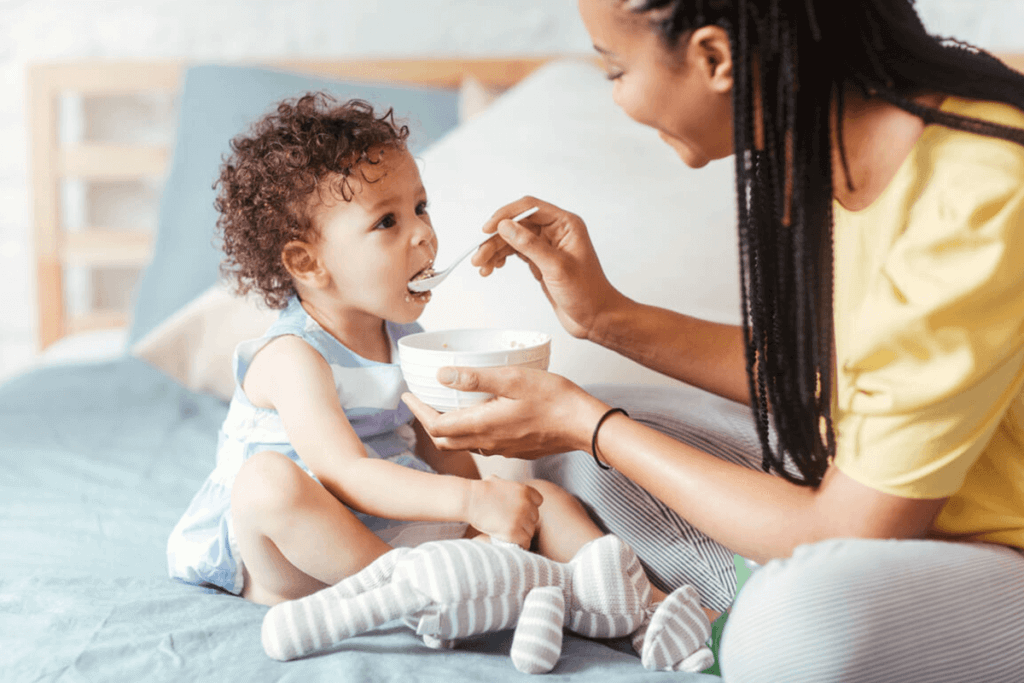 Young mother feeding her daughter on a bed.