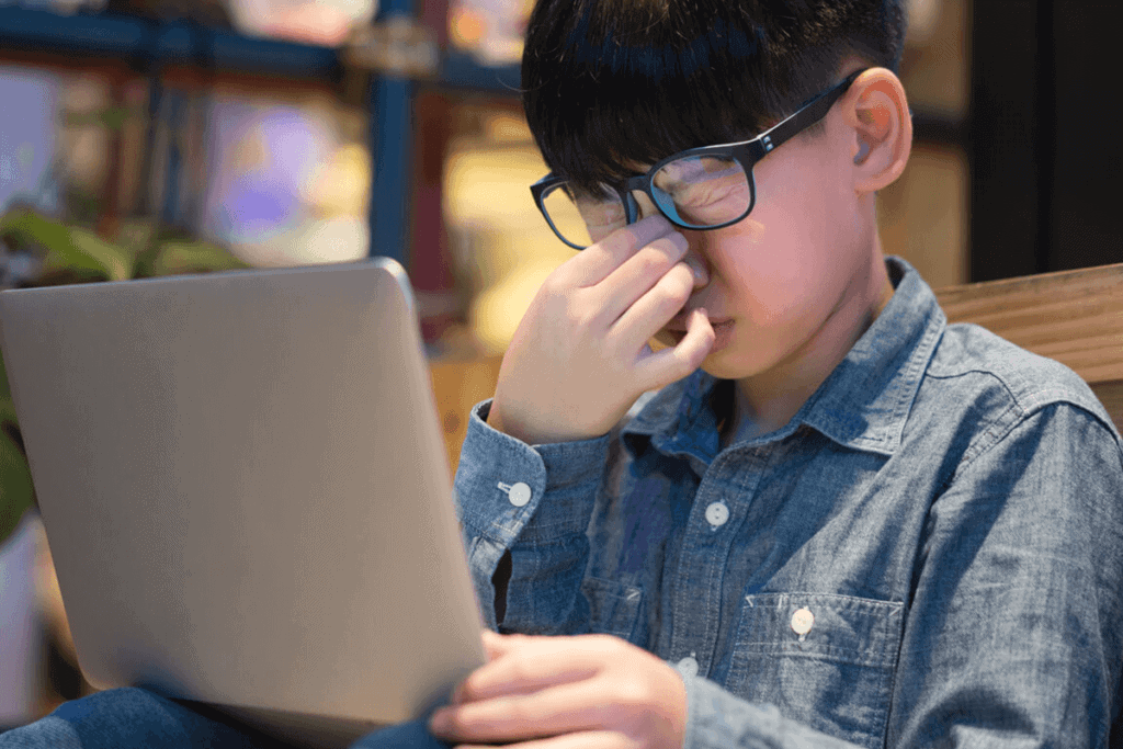 child touching upper part of nose due to eyes hurting