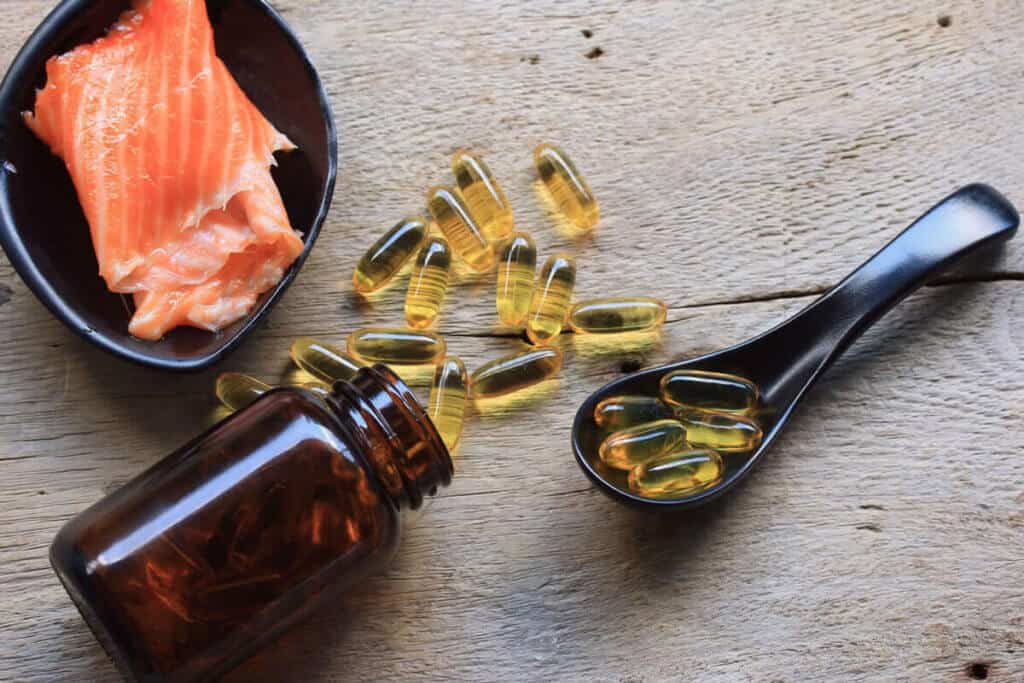 raw salmon in a black dish with omega 3 supplements on a table