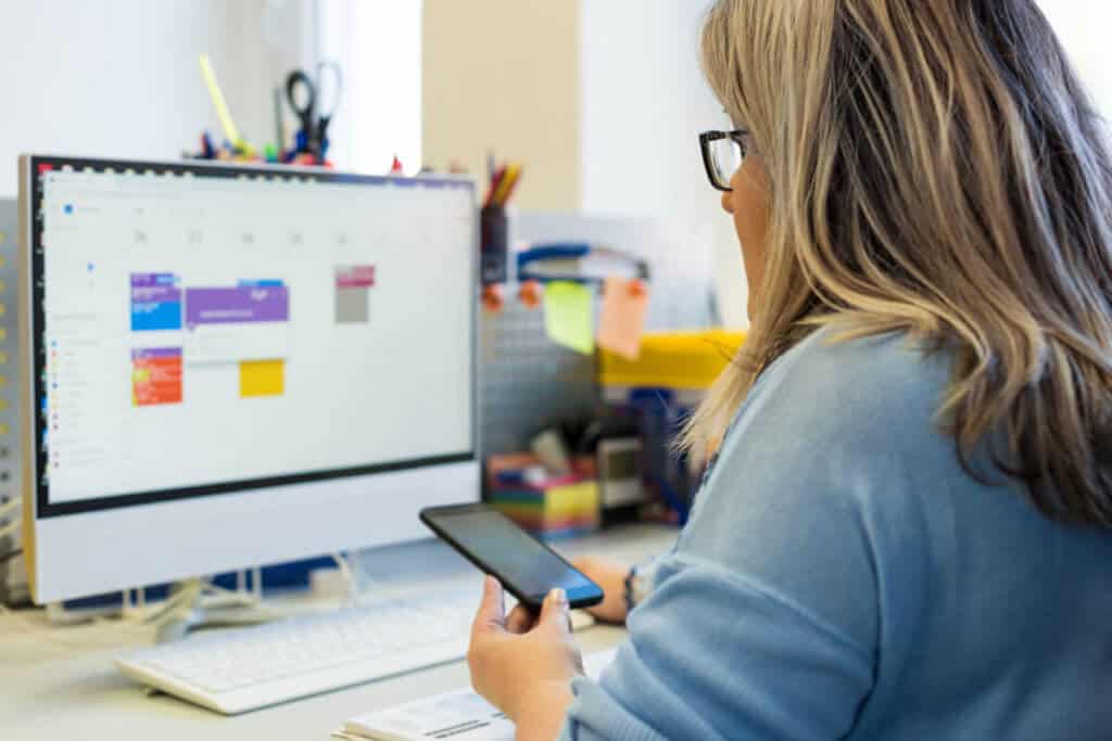 woman looking at her calendar on computer screen while holding a phone