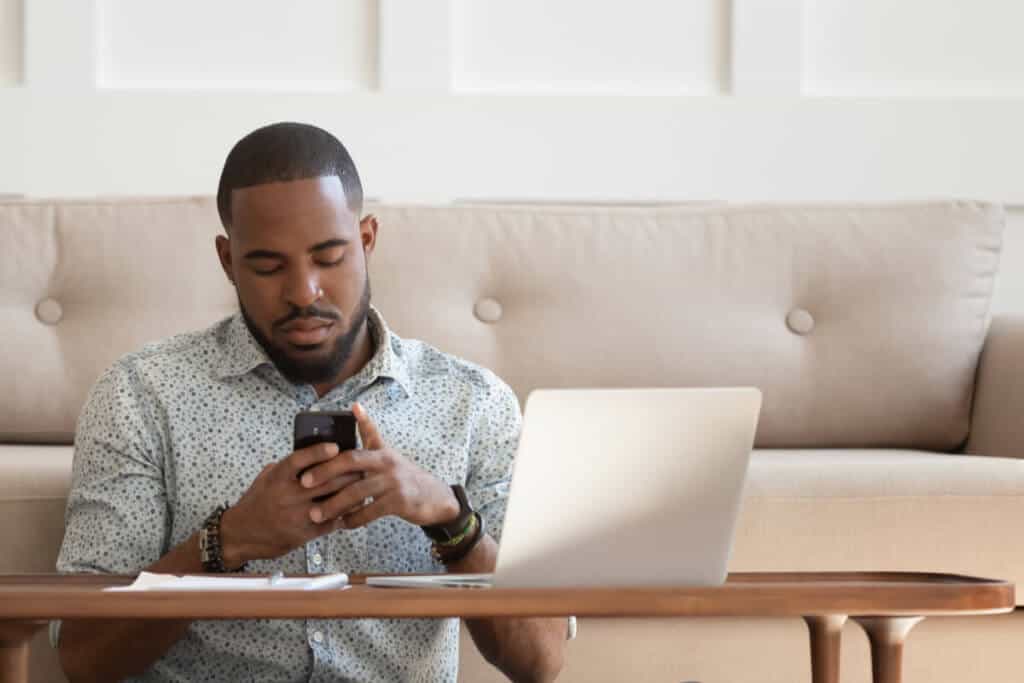 man sitting on floor in living room in front of laptop while he is on the phone