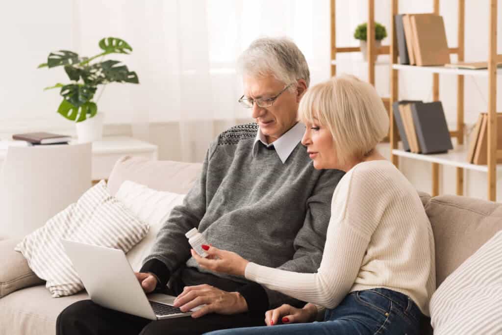 man and woman sitting on couch holding a supplement bottle and computer