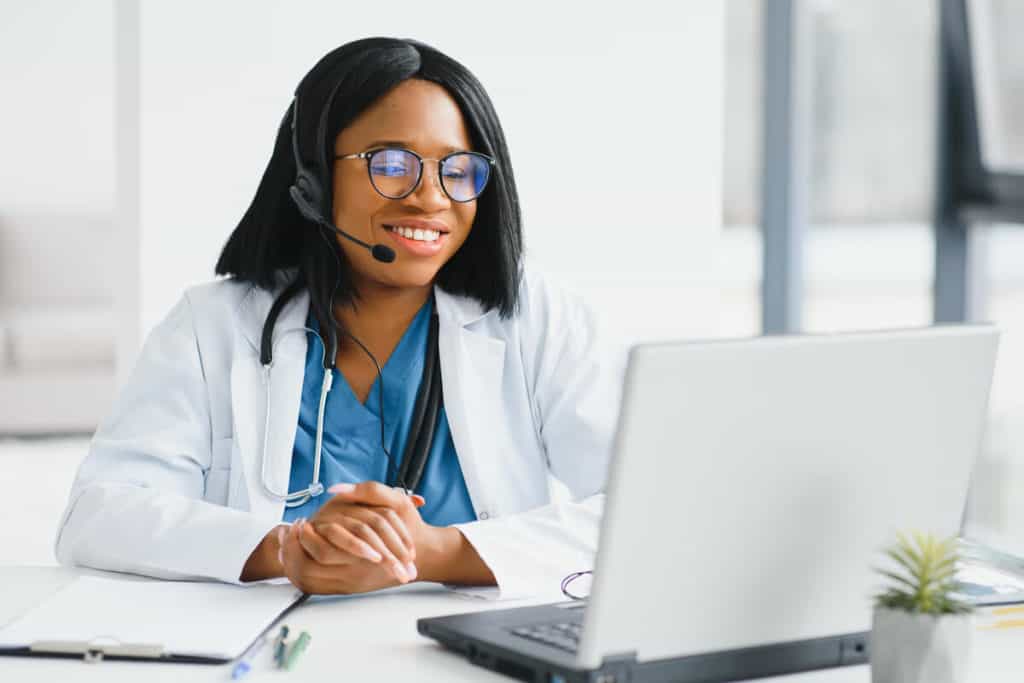 woman practitioner with a headset smiling at laptop